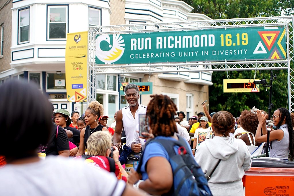 A smiling runner at the Run Richmond 16.19 finish arch on a Richmond street