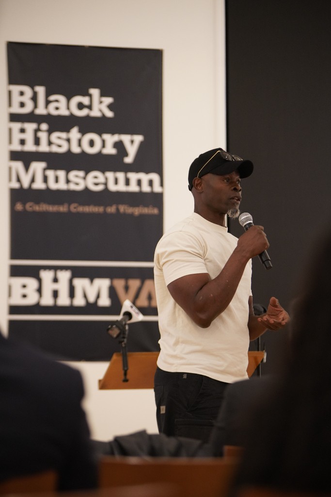 Djimon Hounsou speaking into a handheld microphone at the Black History Museum & Cultural Center of Virginia