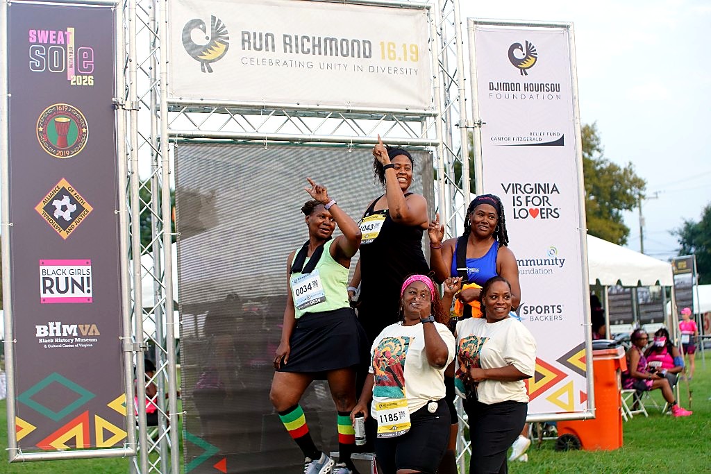 Five runners posing on a step-and-repeat arch bearing Run Richmond 16.19, Sweat With Your Sole, Black Girls RUN, and Djimon Hounsou Foundation banners