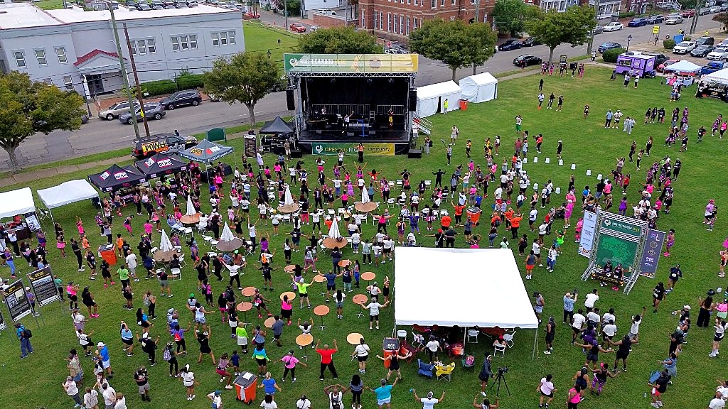 Aerial view of hundreds of participants exercising and warming up together on the grass at Abner Clay Park